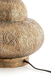 Nahaufnahme eines kunstvoll verzierten Lampenfußes aus Metall mit filigranen Mustern und einem Kabel, seitliche Perspektive.