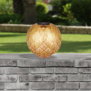 Runde Solarleuchte mit dekorativem Muster, auf einer Steinmauer im Freien platziert, seitliche Perspektive