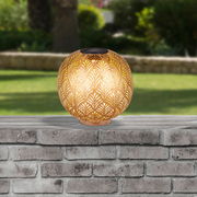 Runde Solarleuchte mit dekorativem Muster, auf einer Steinmauer im Freien platziert, seitliche Perspektive