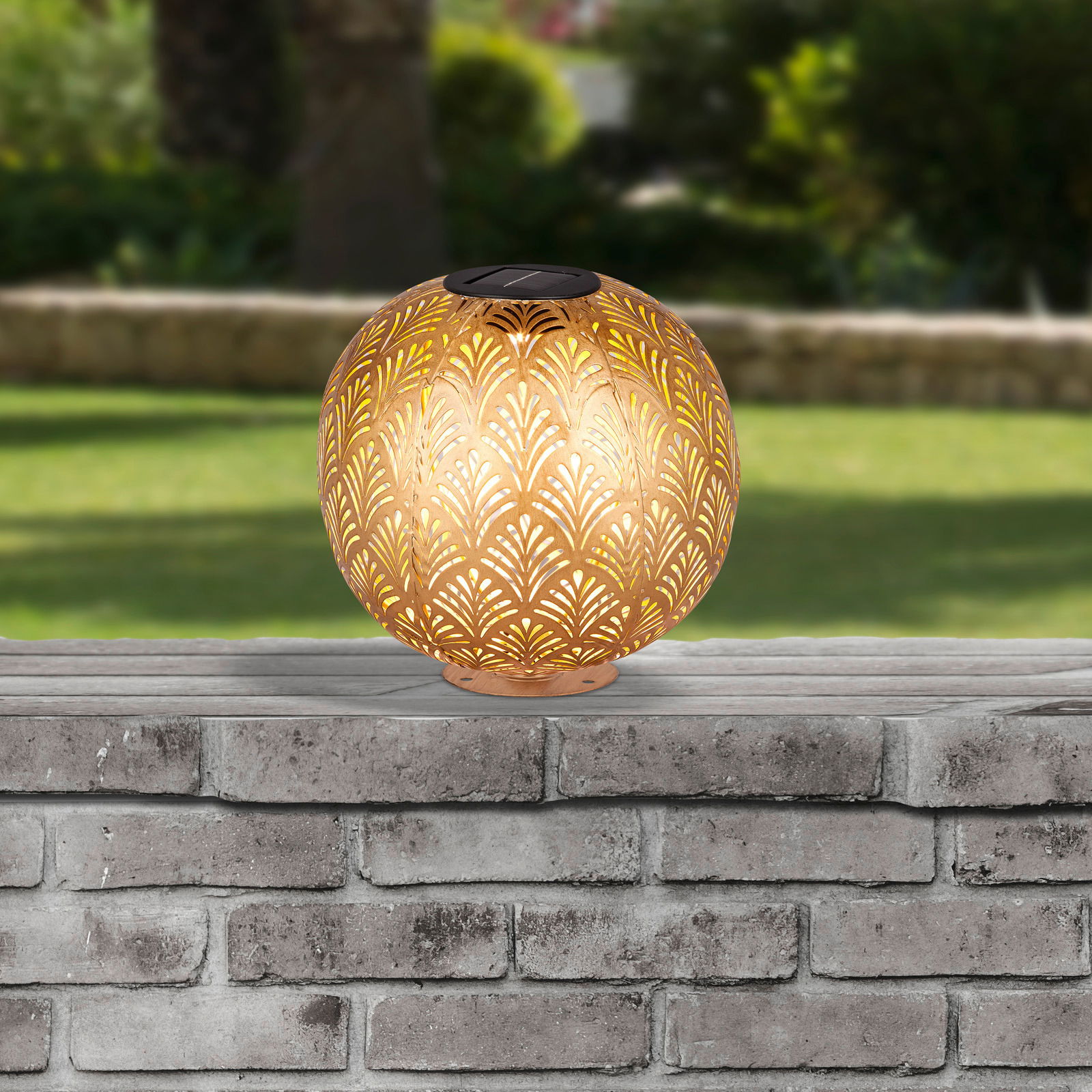 Runde Solarleuchte mit dekorativem Muster, auf einer Steinmauer im Freien platziert, seitliche Perspektive