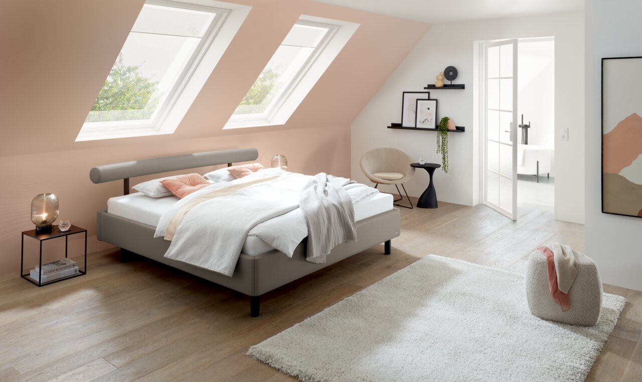 Modernes Polsterbett in einem stilvollen Schlafzimmer mit Dachfenstern, seitliche Perspektive.