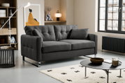 Dunkelgraues, gepolstertes 2-Sitzer-Sofa mit Steppnähten, breiten Armlehnen und verchromten Kufenfüßen im modernen Wohnzimmer, Perspektive: frontale Ansicht leicht von links.