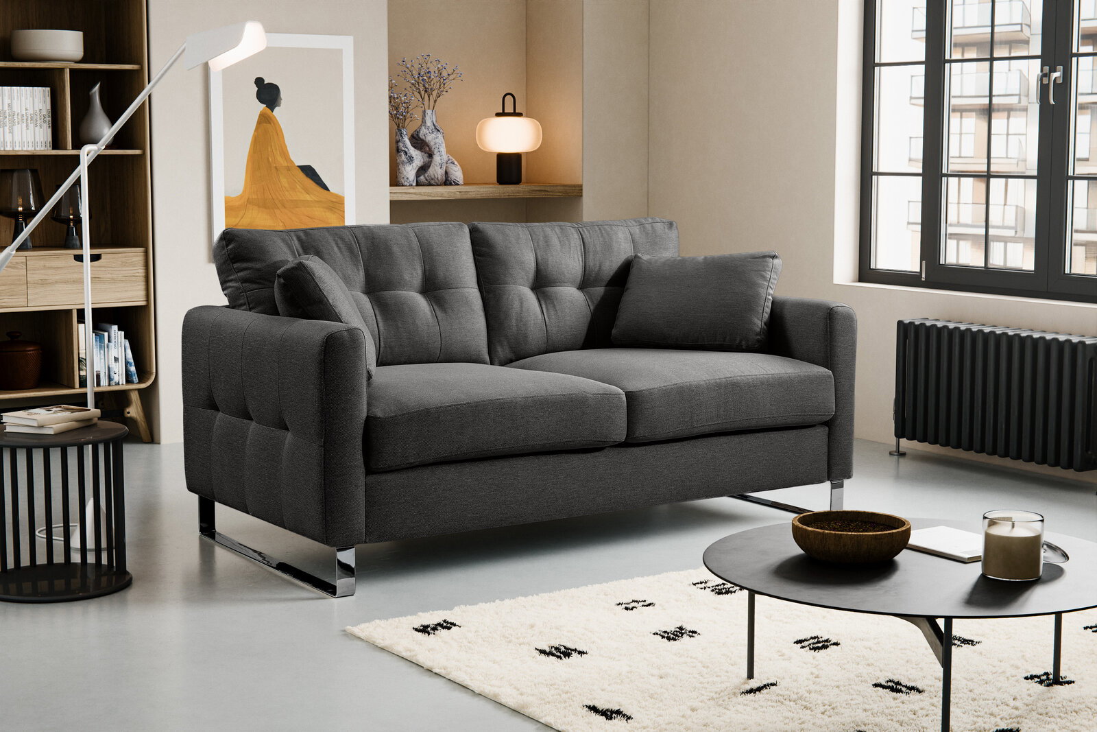 Dunkelgraues, gepolstertes 2-Sitzer-Sofa mit Steppnähten, breiten Armlehnen und verchromten Kufenfüßen im modernen Wohnzimmer, Perspektive: frontale Ansicht leicht von links.