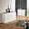 Modernes weißes Sideboard mit drei Schubladen und zwei Türen, in einem stilvoll eingerichteten Raum mit Holzboden und gemustertem Teppich, aus einer seitlichen Perspektive fotografiert.