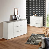 Modernes weißes Sideboard mit drei Schubladen und zwei Türen, in einem stilvoll eingerichteten Raum mit Holzboden und gemustertem Teppich, aus einer seitlichen Perspektive fotografiert.