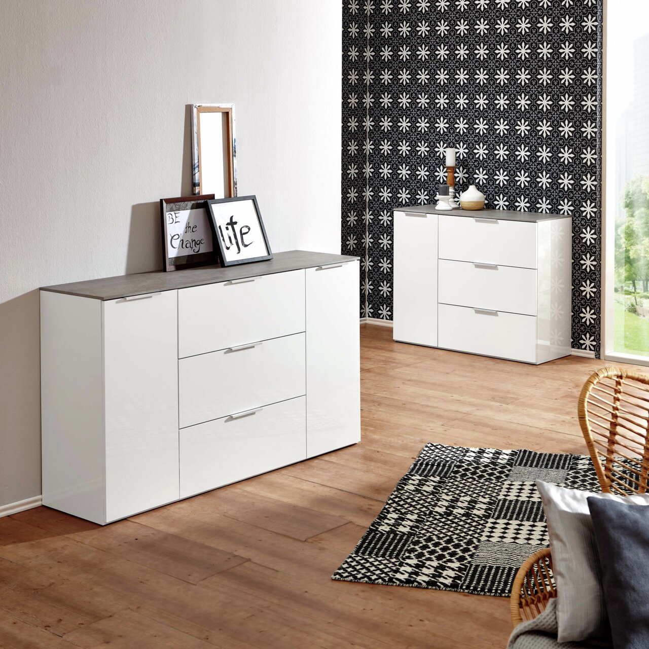 XORA Dressoir GALANT Modern wit dressoir met drie lades en twee deuren, in een stijlvol ingerichte kamer met houten vloer en een tapijt met patroon, gefotografeerd vanuit een zijdelingse hoek.