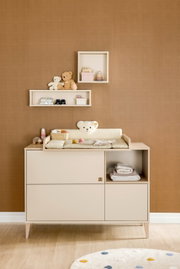 Vooraanzicht van een vierkante wandkast, versierd met speelgoed en accessoires, tegen een bruine muur boven een commode.