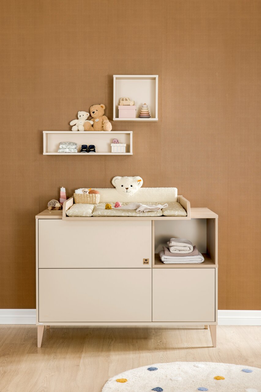 Vooraanzicht van een vierkante wandkast, versierd met speelgoed en accessoires, tegen een bruine muur boven een commode.