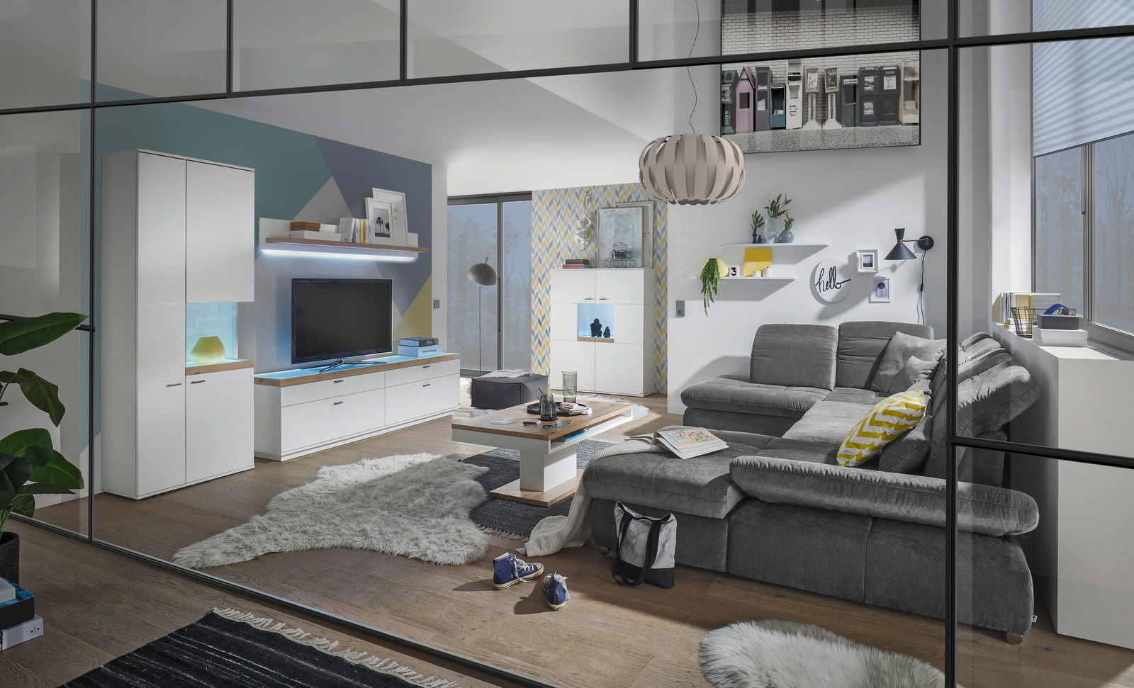 Moderne Wohnzimmeransicht mit grauem Sofa, Couchtisch und TV-Lowboard in einem stilvollen, hellen Raum mit großen Fenstern.