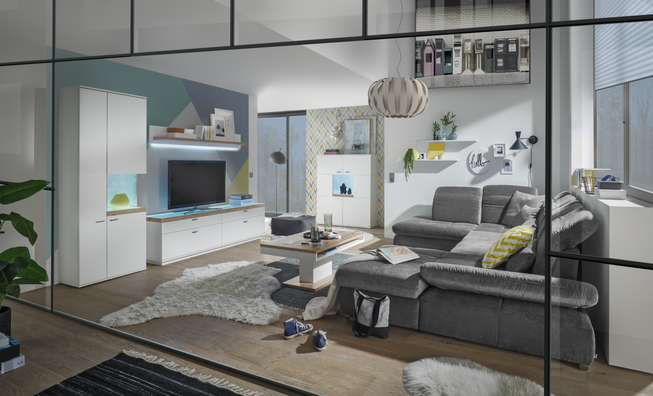 Set one by Musterring Vitrine Glasausschnitt rechts SET ONE LANCASTER Moderne Wohnzimmeransicht mit grauem Sofa, Couchtisch und TV-Lowboard in einem stilvollen, hellen Raum mit großen Fenstern.