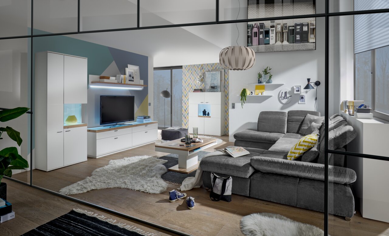 Moderne Wohnzimmeransicht mit grauem Sofa, Couchtisch und TV-Lowboard in einem stilvollen, hellen Raum mit großen Fenstern.