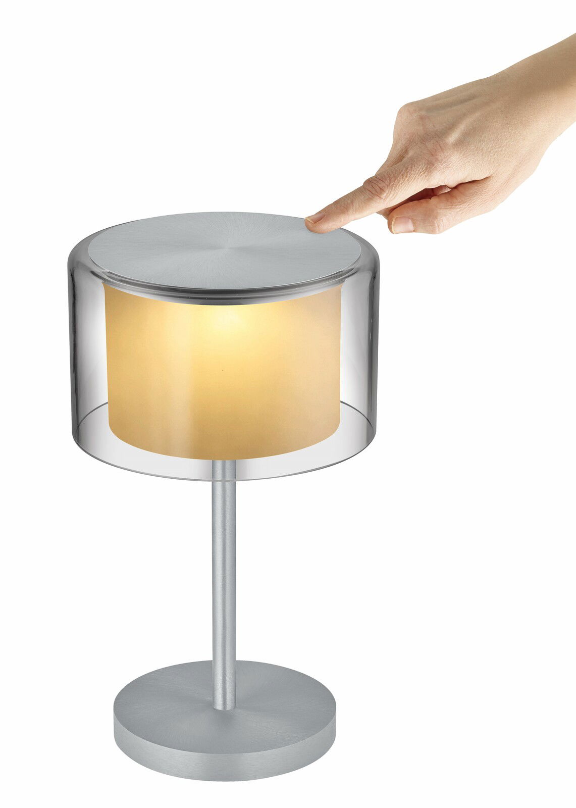 Akku-Tischleuchte GRAND SMOKE mit transparentem Schirm und silbernem Sockel, seitliche Perspektive, Hand berührt den oberen Teil der Leuchte.