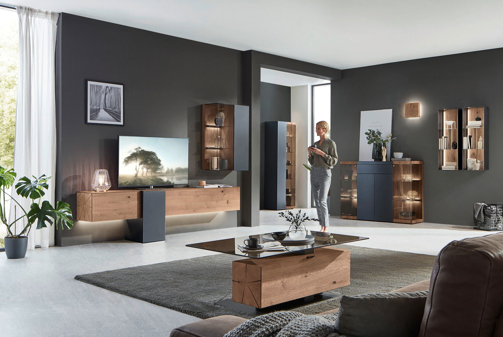 Moderne Wohnzimmer-Wandkombination in Holzoptik mit integrierter Beleuchtung, aus der Perspektive eines offenen, hellen Raumes betrachtet.