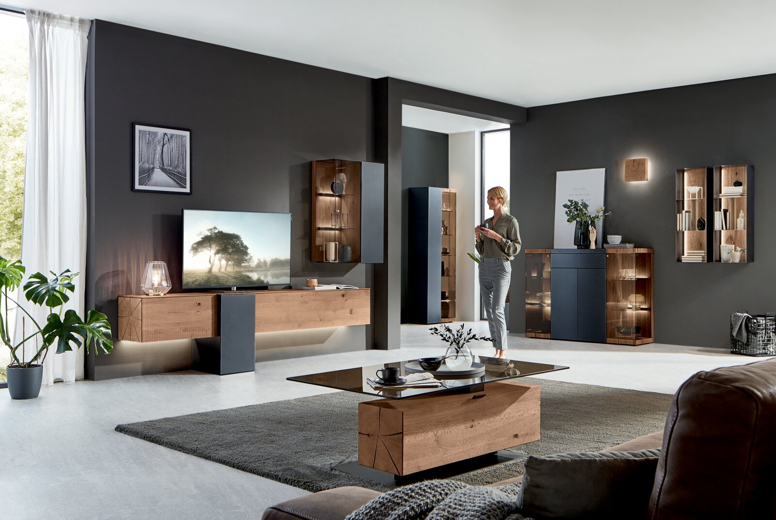 Moderne Wohnzimmer-Wandkombination in Holzoptik mit integrierter Beleuchtung, aus der Perspektive eines offenen, hellen Raumes betrachtet.