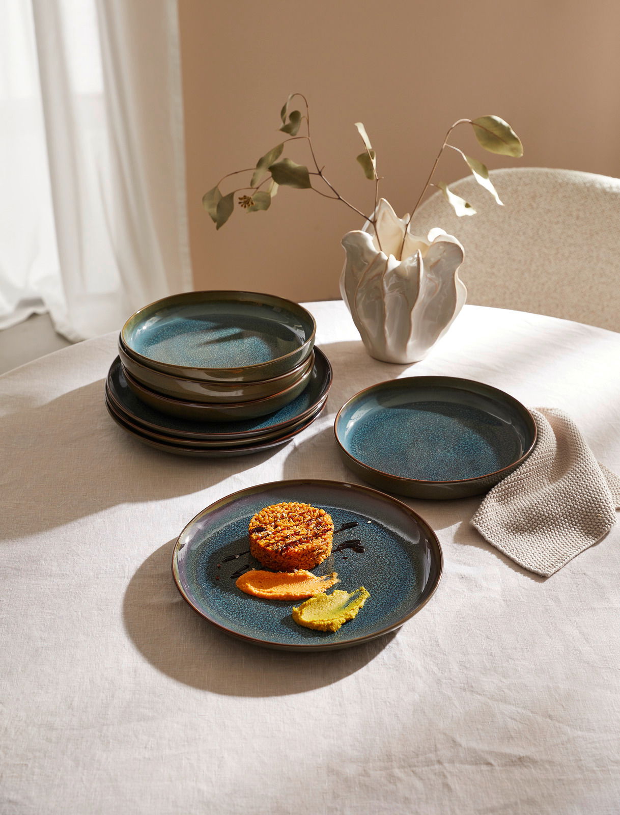 Like by Villeroy & Boch Tafelset 8-tlg. CRAFTED BREEZE Ein Tafelset mit acht Teilen namens Breeze, bestehend aus eleganten, blauen Tellern auf einem Tisch. Die Perspektive zeigt die Teller von oben, mit einem dekorativen Gericht auf einem der Teller und einer stilvollen Vase im Hintergrund.