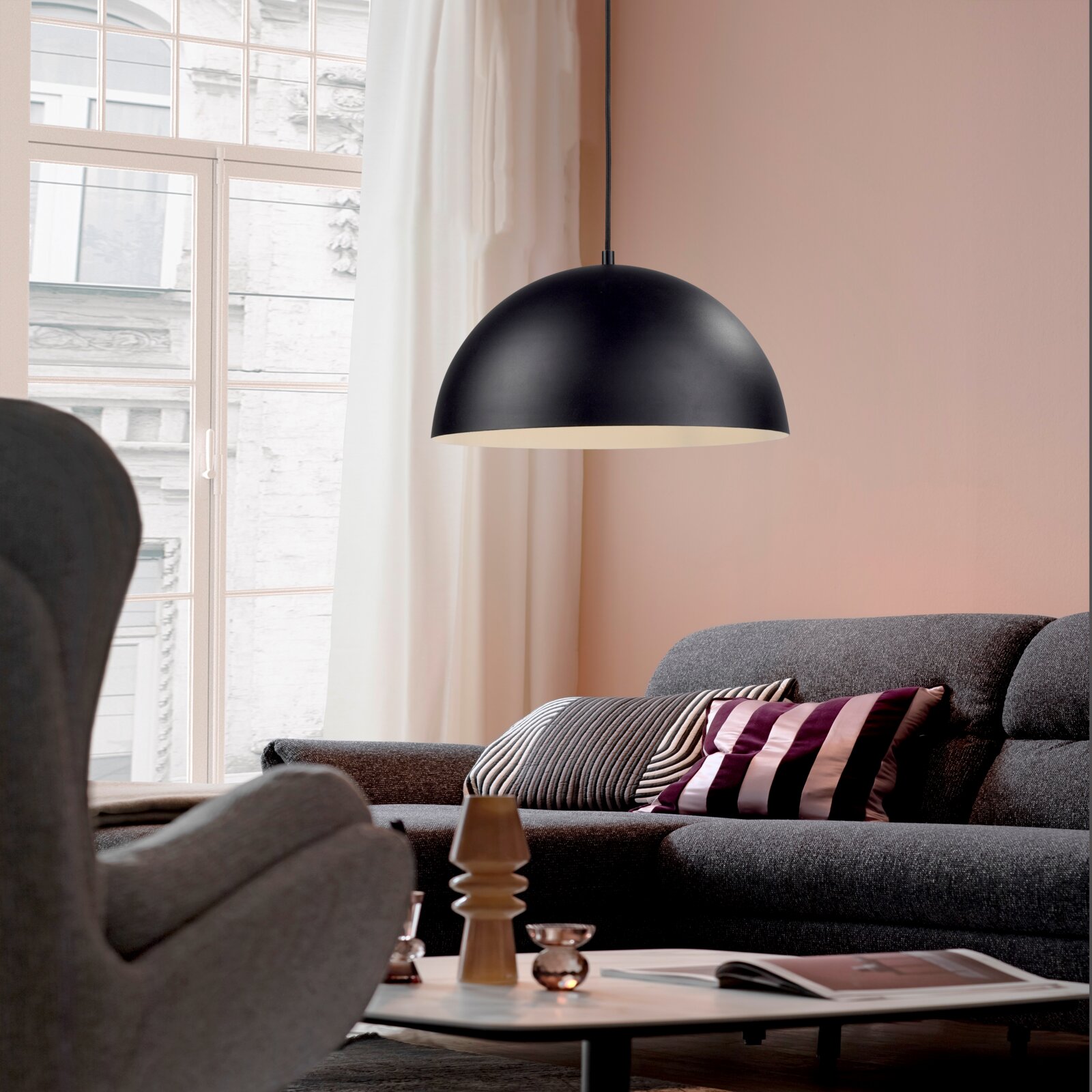Schwarze, halbkugelförmige Pendelleuchte mit matter Oberfläche über grauem Sofa im Wohnzimmer, Seitenansicht leicht von unten