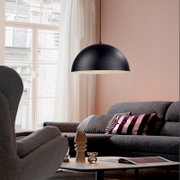 Schwarze, halbkugelförmige Pendelleuchte mit matter Oberfläche über grauem Sofa im Wohnzimmer, Seitenansicht leicht von unten