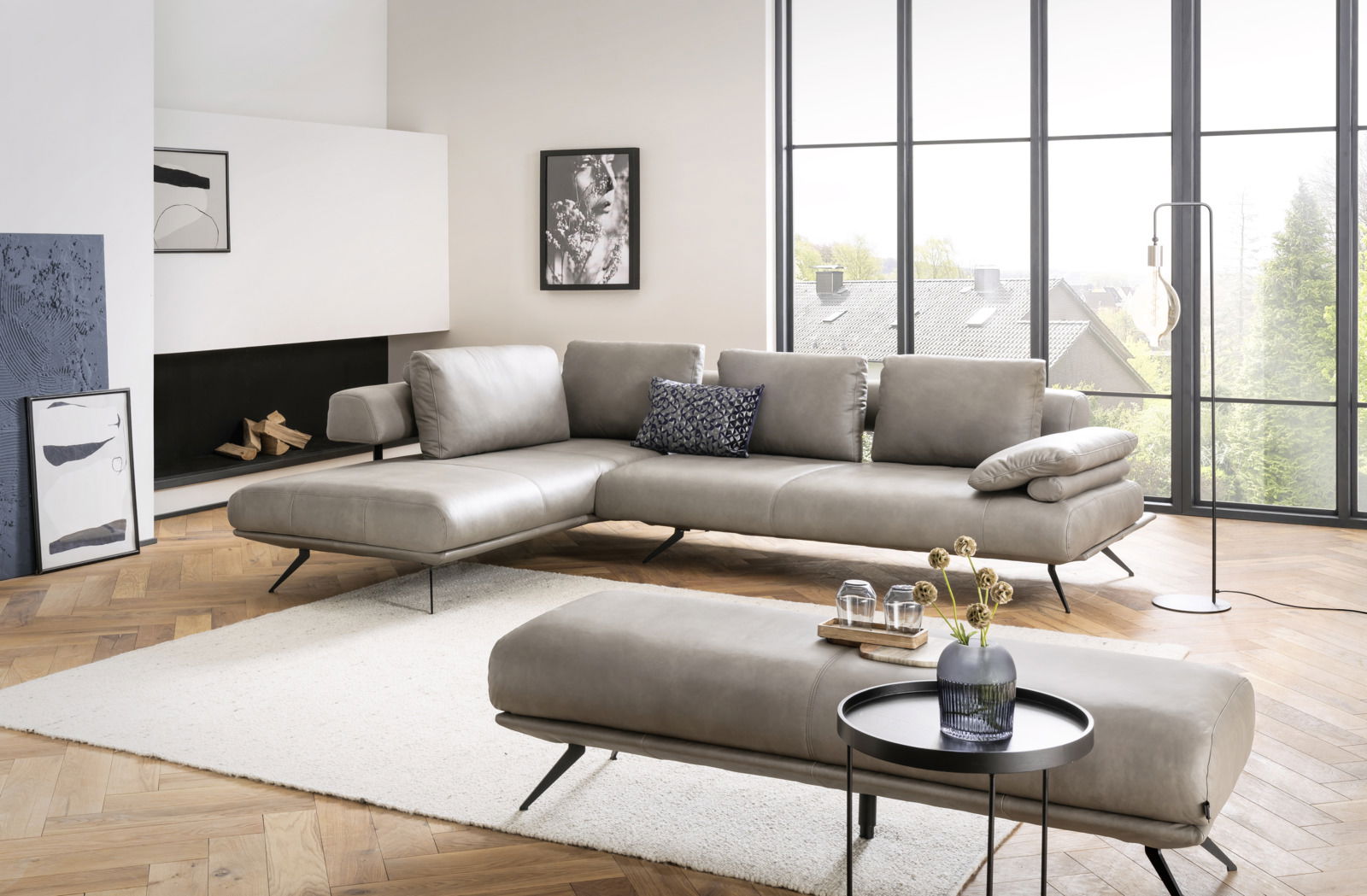 Dieter Knoll Hocker medium MARANELLO 2.0 Moderne Eckgarnitur in einem hellen Wohnzimmer mit großen Fenstern, aus der Perspektive von vorne rechts betrachtet.