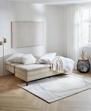 Querschläfer-Sofa in einem hellen Raum, seitliche Perspektive, mit Kissen und Decke dekoriert, auf einem Teppich stehend.