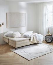 Querschläfer-Sofa in einem hellen Raum, seitliche Perspektive, mit Kissen und Decke dekoriert, auf einem Teppich stehend.