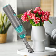 Kabelloser Handstaubsauger Invictus One Home in modernem Design, schwebend über einem Tisch mit einer Vase voller rosa Tulpen, seitliche Perspektive.