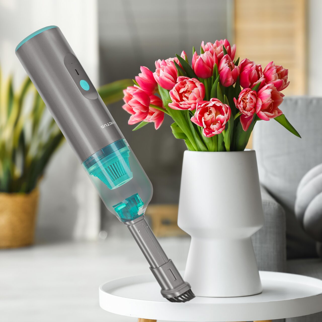 Genius Invictus One Home, 8-delige set De draadloze handstofzuiger Invictus One Home in een modern ontwerp, zwevend boven een tafel met een vaas vol roze tulpen, gezien vanuit een zijdelingse hoek.