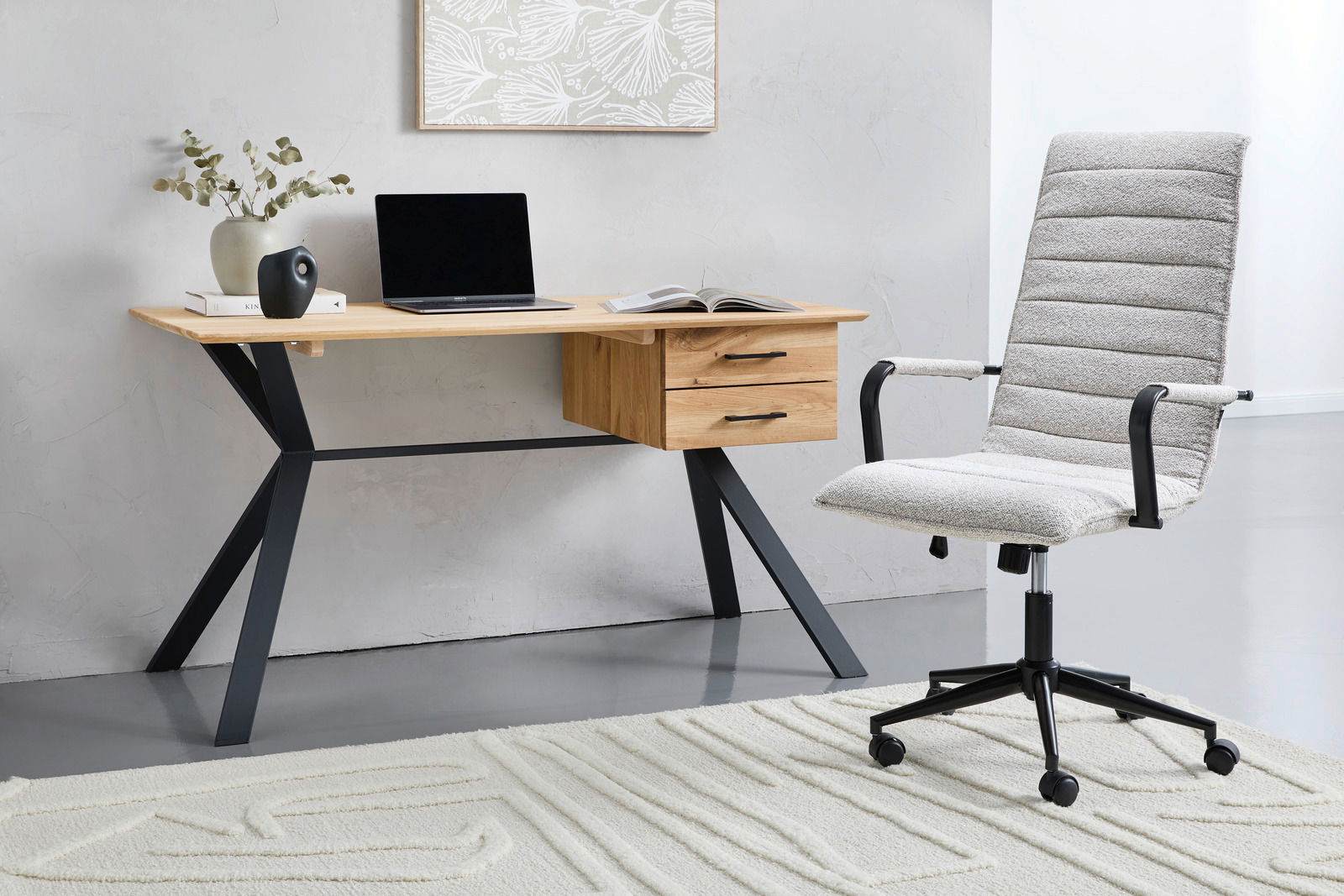 Moderner Schreibtisch mit Holzplatte und schwarzen Metallbeinen, seitlich mit Schubladen, aus der Perspektive von vorne rechts fotografiert. Daneben steht ein gepolsterter Bürostuhl auf einem Teppich.