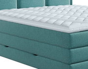 Close-up van een turkoois boxspringbed met een gewatteerde topper, gezien vanaf de zijkant
