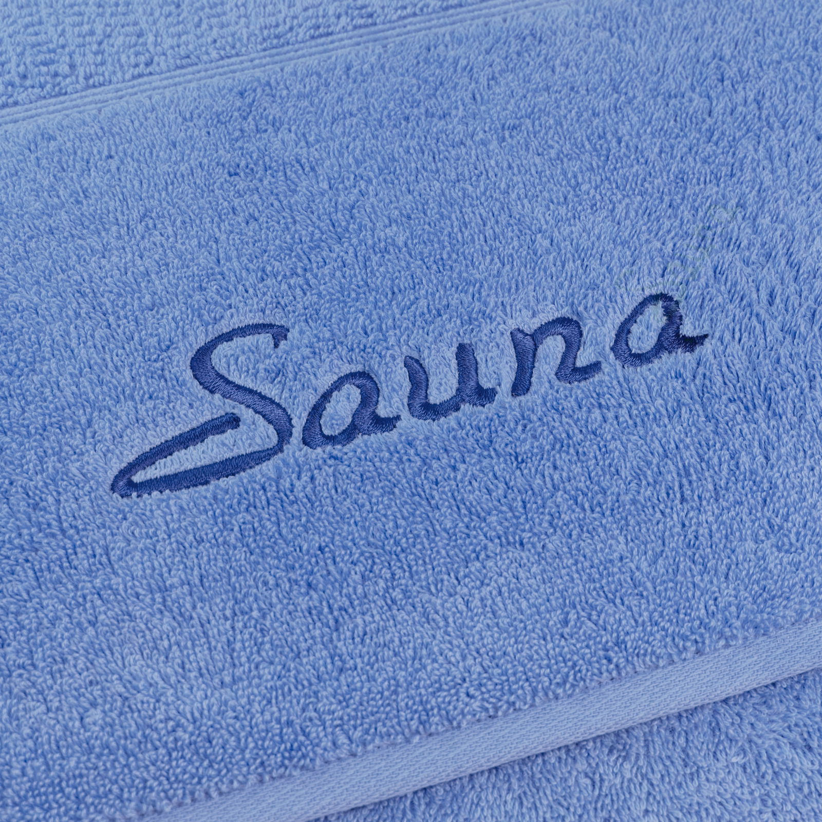 MÖVE Saunatuch 2er-Set PEARL Nahaufnahme eines blauen Saunatuchs mit gesticktem Schriftzug 'Sauna'.