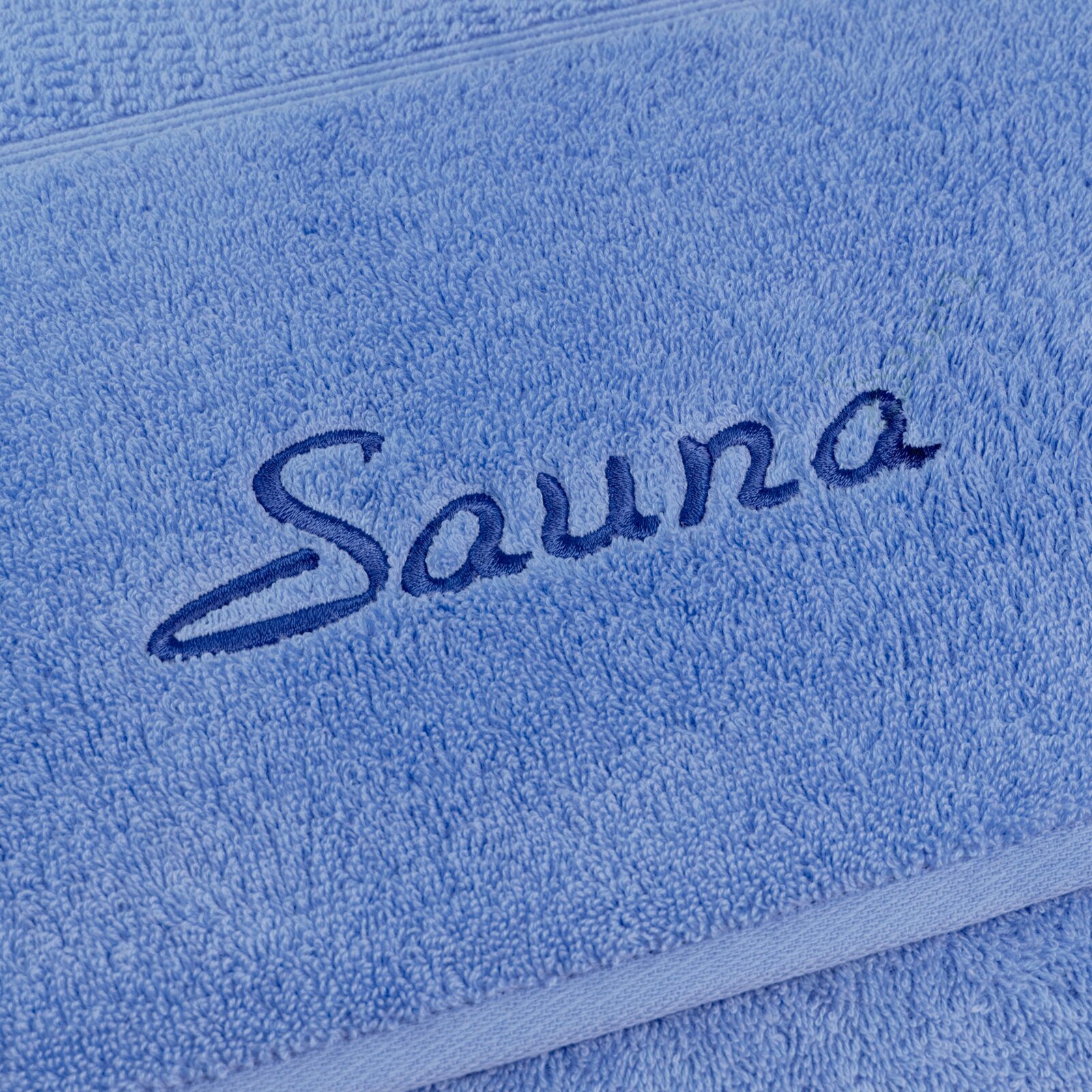 MÖVE Set van 2 saunadoeken PEARL Nahaufnahme eines blauen Saunatuchs mit gesticktem Schriftzug 'Sauna'.