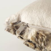 Nahaufnahme eines Kissens mit weicher, beiger Oberfläche und einem Reißverschluss an der Seite, umgeben von einem flauschigen, gemusterten Rand.