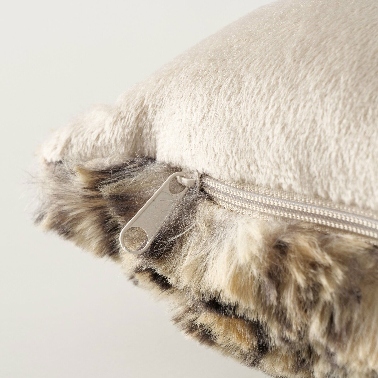 Nahaufnahme eines Kissens mit weicher, beiger Oberfläche und einem Reißverschluss an der Seite, umgeben von einem flauschigen, gemusterten Rand.