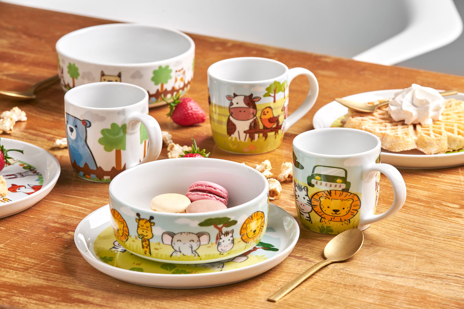 Kinderset mit Safari-Motiven, bestehend aus Tassen und Schalen, auf einem Holztisch arrangiert, mit Blick von oben.