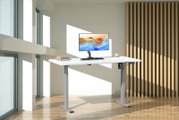 Höhenverstellbarer Schreibtisch mit weißer Tischplatte und grauem Metallgestell, mit Monitor, Tastatur und Büchern in modernem, lichtdurchflutetem Büro – Perspektive: frontale leicht seitliche Ansicht.