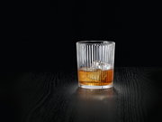 Ein elegantes, geripptes Glas mit einem Getränk und Eiswürfeln, auf einem dunklen Tisch aus der Seitenperspektive fotografiert.