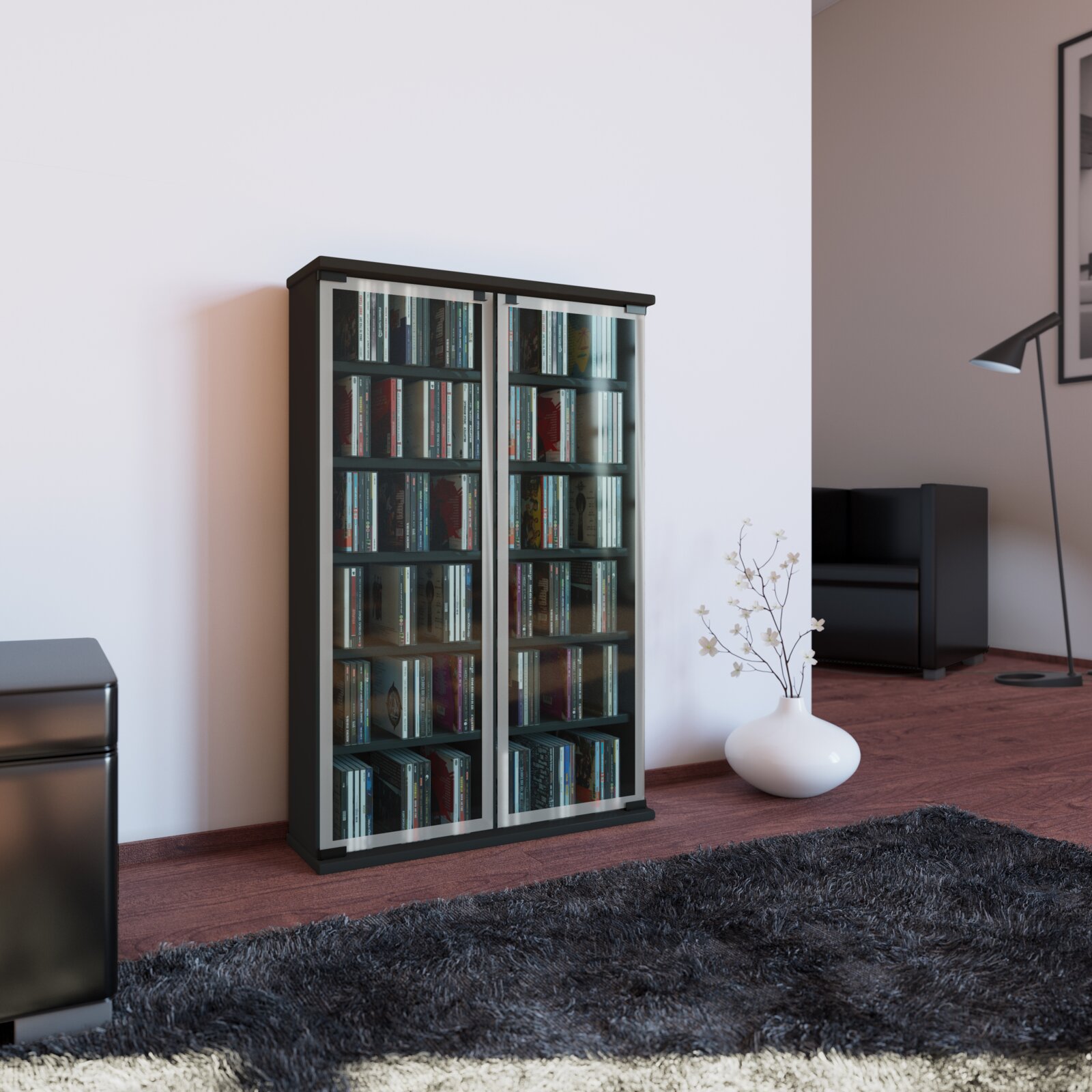 Schwarzer CD-/DVD-Schrank mit zwei Glas-Schiebetüren und silbernen Rahmen, gefüllt mit CDs, im Wohnzimmer vor weißer Wand – frontale Ansicht mit leichter Perspektive von links.