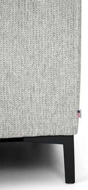 Nahaufnahme einer grauen, texturierten Stoffoberfläche eines Möbels mit schwarzem Metallfuß, seitliche Perspektive.