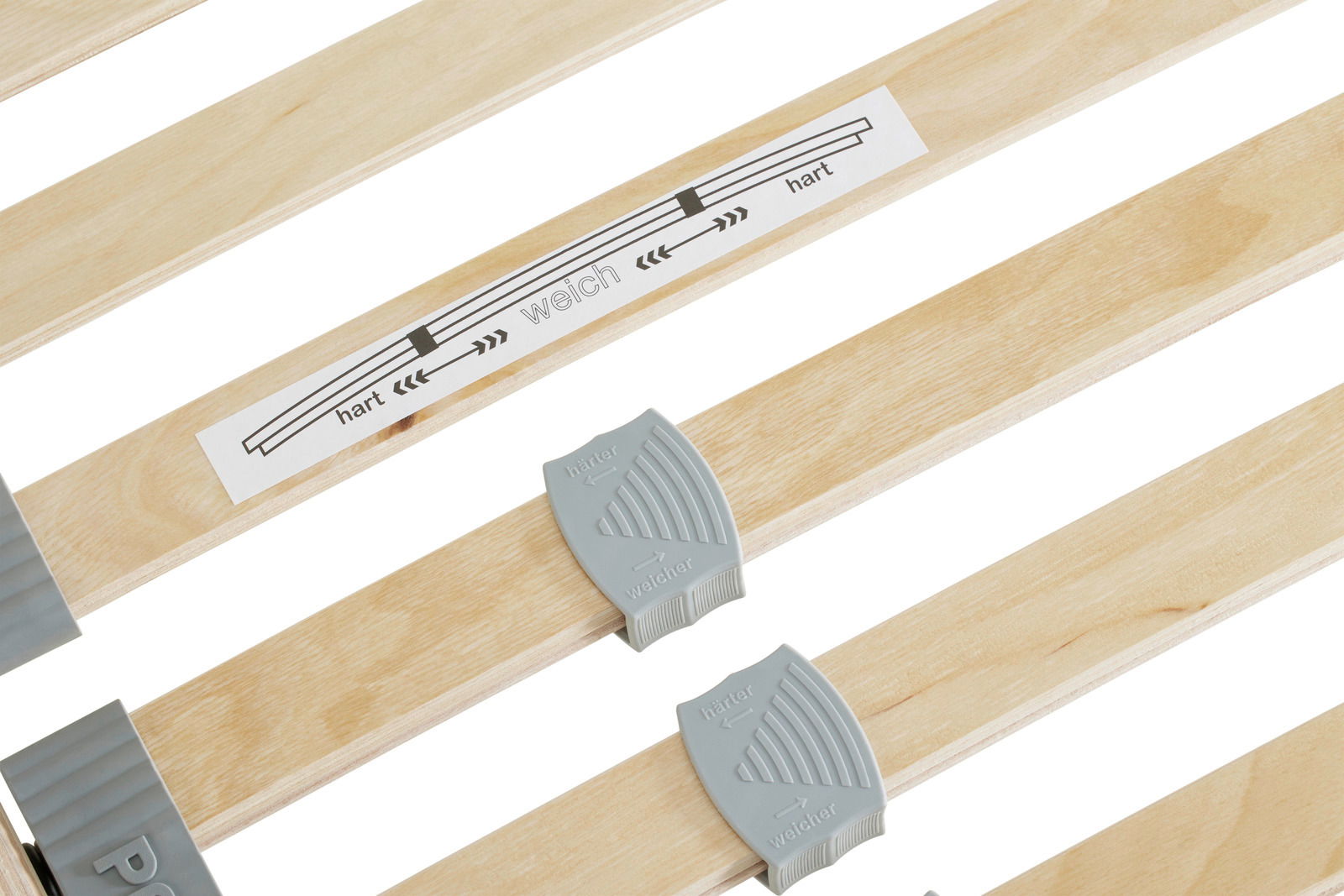 Nahaufnahme eines Federholzrahmens mit verstellbaren Härtegradreglern und Beschriftung 'hart' und 'weich'.