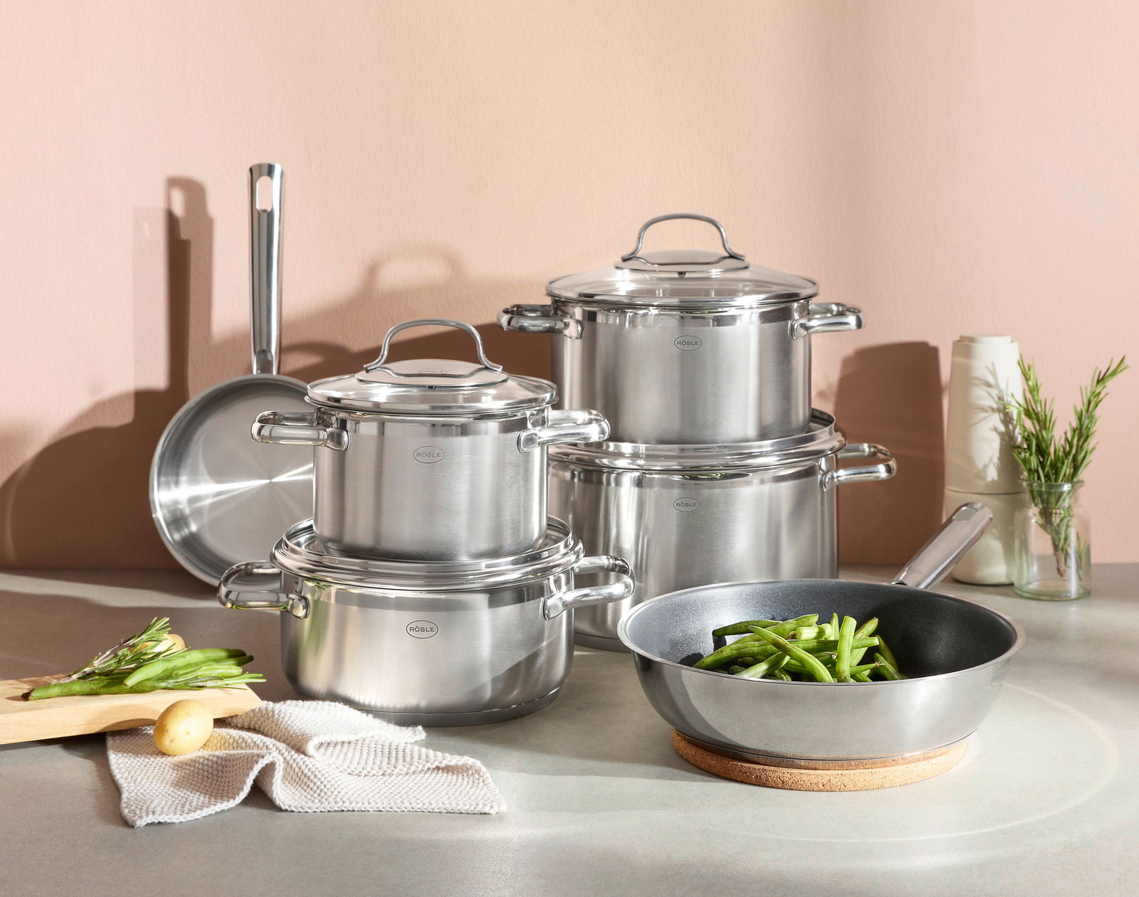 Topfset ELEGANCE 6-tlg. aus Edelstahl, bestehend aus mehreren Töpfen und Pfannen, auf einer Küchenarbeitsplatte arrangiert. Perspektive von vorne.