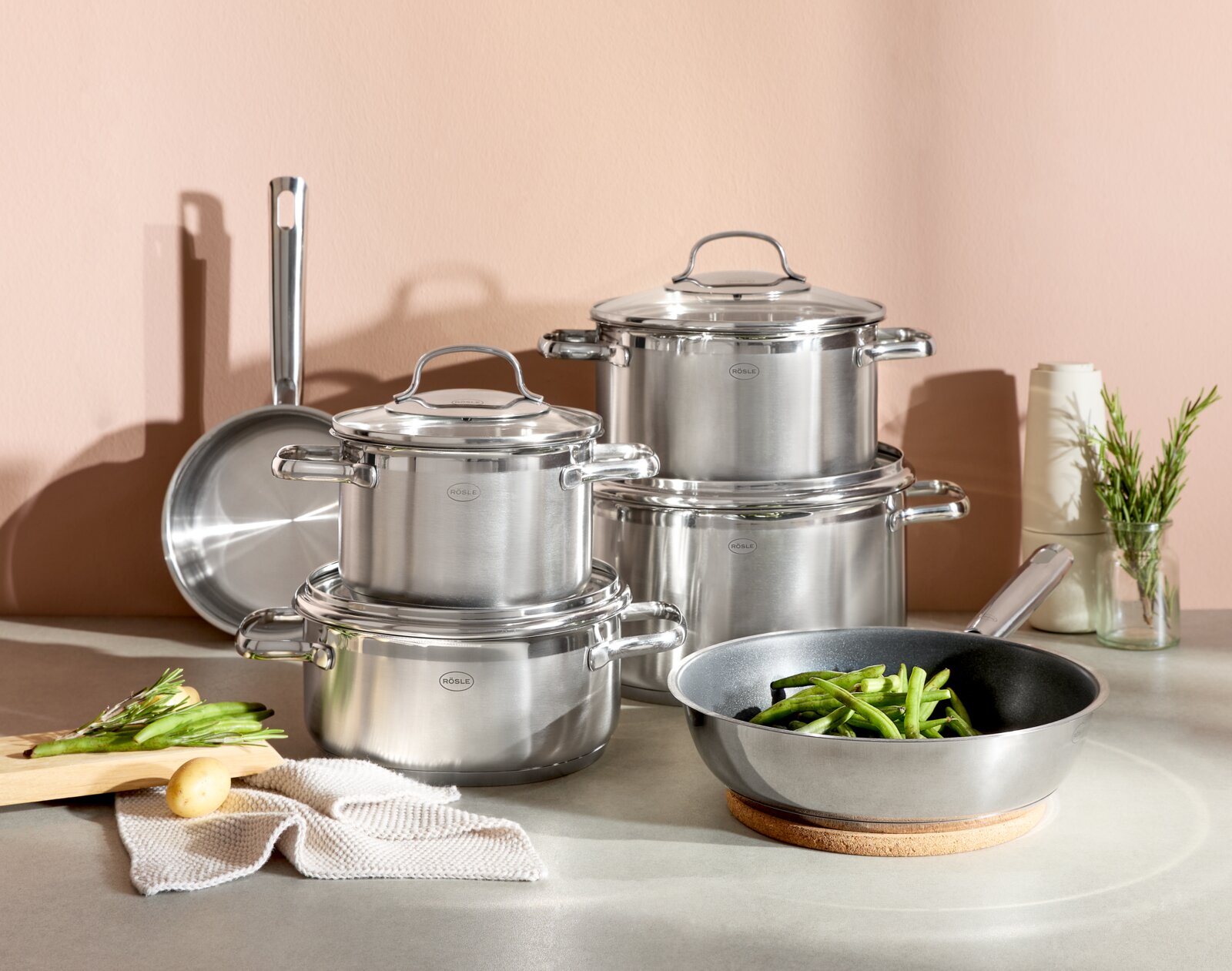 Topfset ELEGANCE 6-tlg. aus Edelstahl, bestehend aus mehreren Töpfen und Pfannen, auf einer Küchenarbeitsplatte arrangiert. Perspektive von vorne.