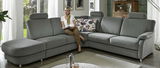 Graues Ecksofa TAULON-S in einem modernen Wohnzimmer, mit einer Person, die darauf sitzt. Perspektive von vorne links.