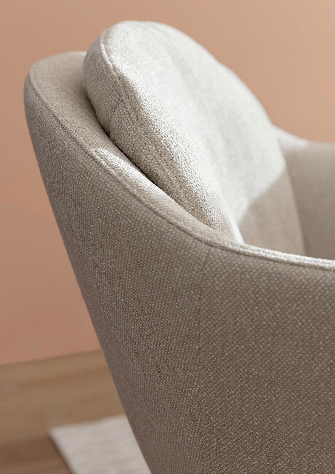 Nahaufnahme eines beigen Armlehnstuhls mit texturierter Oberfläche, seitliche Perspektive