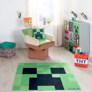 Minecraft Kinderzimmer mit grünem Creeper-Teppich im Vordergrund, Sessel mit Creeper-Kissen und Minecraft-Aufbewahrungswürfeln; Perspektive: frontale Raumansicht auf Augenhöhe.