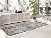 Designer Teppich in einem modernen Wohnzimmer, mit einem bunten, abstrakten Muster in Grau, Rot und Gelb, auf hellem Holzboden vor einem weißen Sideboard. Perspektive von schräg oben.