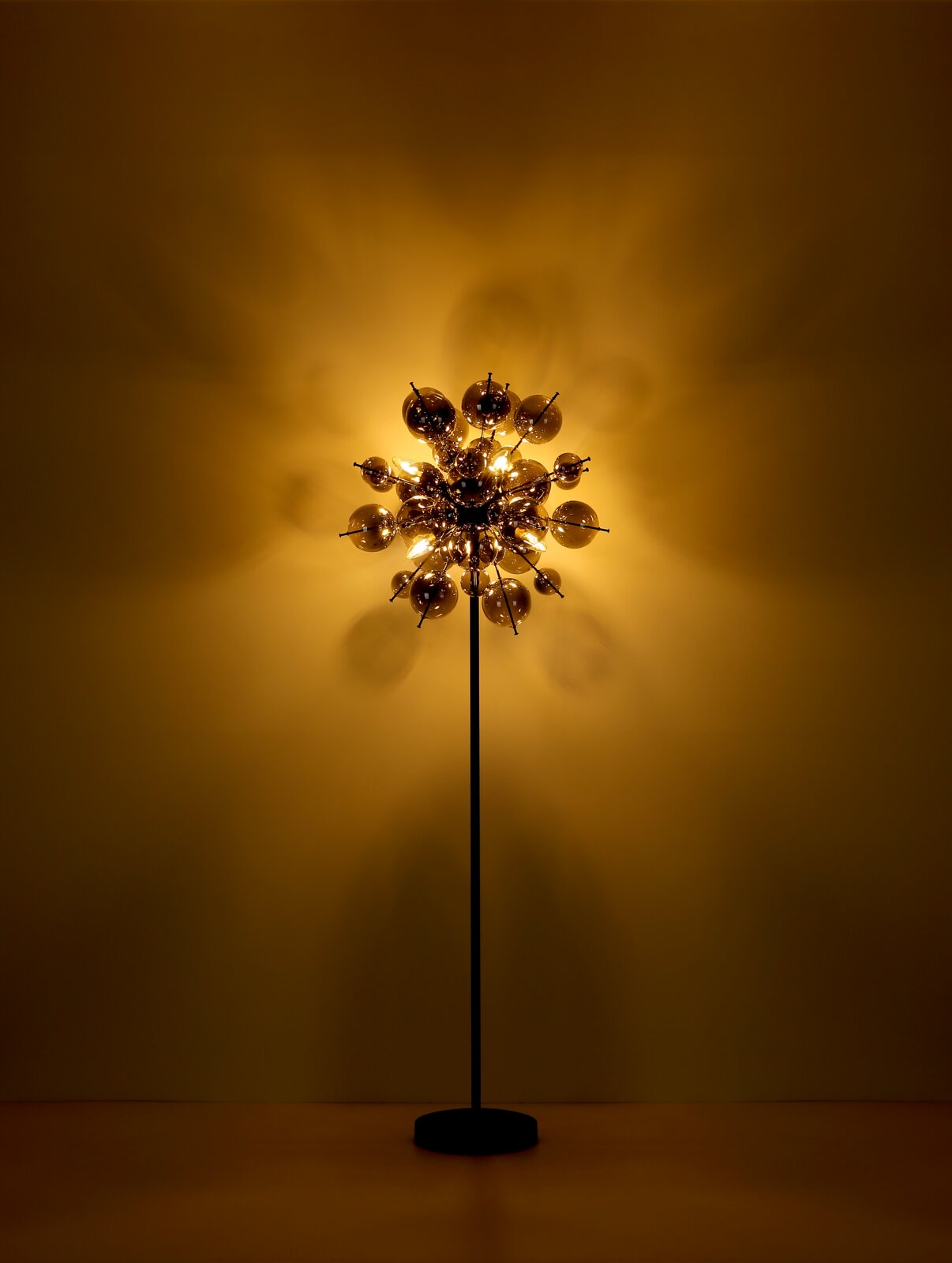 Moderne Stehleuchte mit kugelförmigem Design, beleuchtet in einem warmen, goldenen Licht, frontal betrachtet.