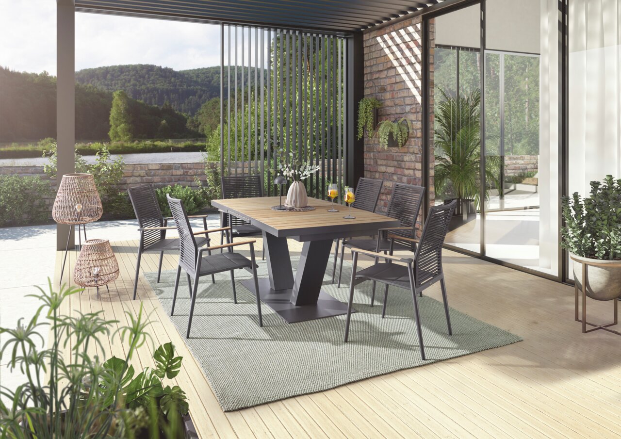 Moderner Essbereich im Freien mit stilvollen Sesseln und einem Tisch auf einer Terrasse mit Blick auf die Natur, aus seitlicher Perspektive.