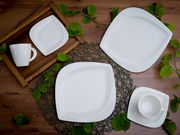 Vogelperspektive auf ein elegantes, weißes Kaffeeservice-Set mit Tassen, Untertassen und Tellern, dekoriert mit grünen Blättern auf einem Holztisch.