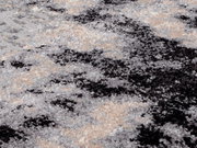 Nahaufnahme eines Designer Teppichs mit abstraktem Muster in Grau-, Schwarz- und Beigetönen, aus seitlicher Perspektive fotografiert.