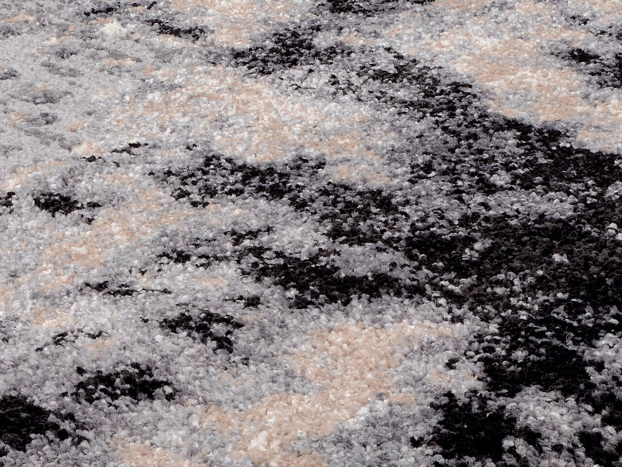 Nahaufnahme eines Designer Teppichs mit abstraktem Muster in Grau-, Schwarz- und Beigetönen, aus seitlicher Perspektive fotografiert.