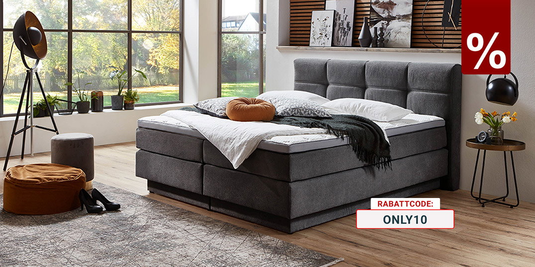 Modern eingerichtetes Schlafzimmer mit grauem Boxspringbett, dekorativer Holzlamellen-Wand, großen Fensterfronten und Blick in den Garten.